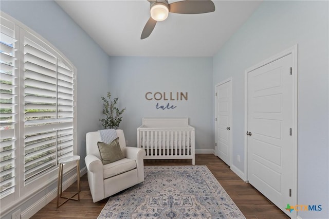 bedroom featuring a crib, baseboards, a ceiling fan, and dark wood finished floors
