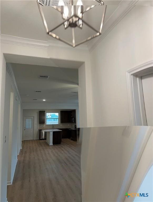 corridor with crown molding, hardwood / wood-style floors, sink, and an inviting chandelier