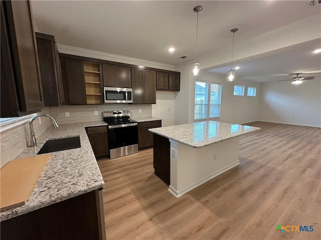 kitchen with ceiling fan, sink, light stone counters, a kitchen island, and appliances with stainless steel finishes