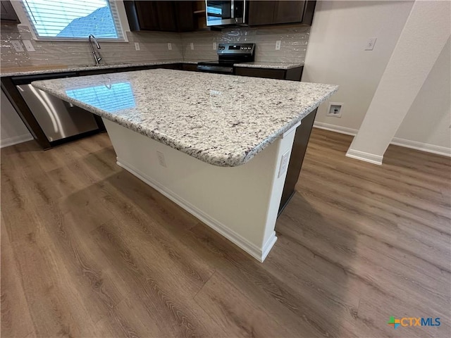 kitchen with light stone countertops, dark brown cabinets, a kitchen island, dark hardwood / wood-style flooring, and stainless steel appliances