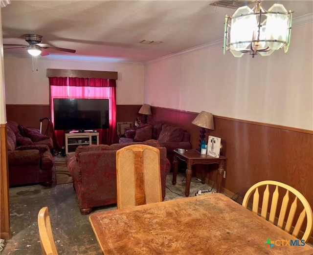 dining space with ceiling fan with notable chandelier, wood walls, crown molding, and concrete floors