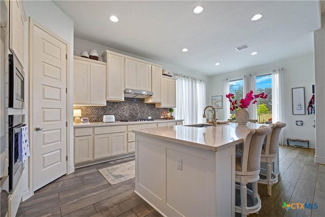 1235 Yaupon Loop, New Braunfels, TX 78132 - kitchen featuring dark wood-style flooring, under cabinet range hood, an island with sink, a breakfast bar, and light countertops