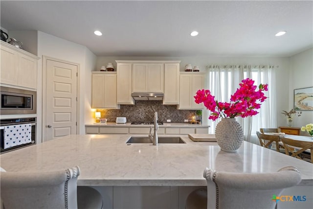 1235 Yaupon Loop, New Braunfels, TX 78132 - kitchen featuring oven, stainless steel microwave, under cabinet range hood, backsplash, and a breakfast bar area