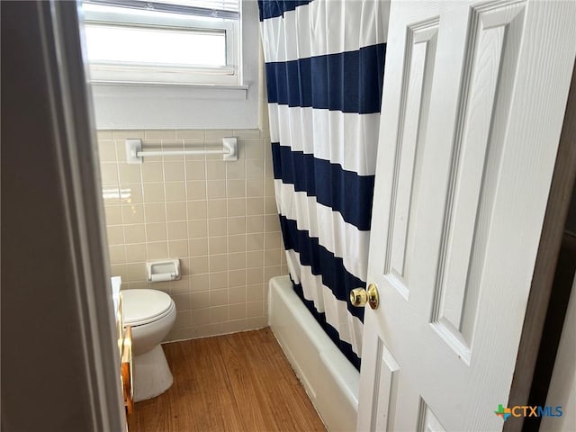 bathroom with toilet, wood finished floors, tile walls, wainscoting, and shower / bath combination with curtain