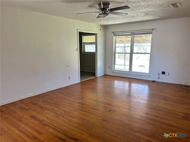 empty room with visible vents, a ceiling fan, a textured ceiling, wood finished floors, and baseboards