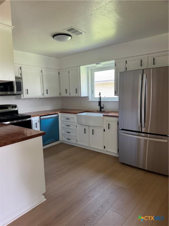 1508 Briar Ln, Killeen, TX 76543 - kitchen featuring appliances with stainless steel finishes, light wood-style flooring, white cabinets, wood counters, and decorative backsplash
