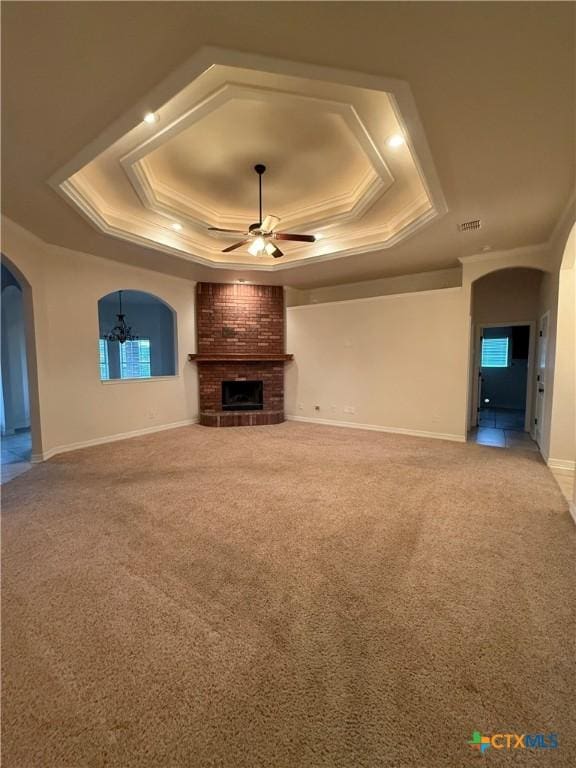 unfurnished living room featuring a fireplace, ceiling fan with notable chandelier, a tray ceiling, and light colored carpet