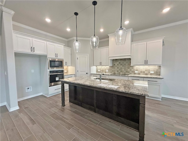 kitchen with a kitchen island with sink, white cabinets, stainless steel appliances, and light wood-type flooring