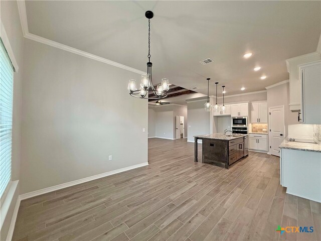 kitchen featuring white cabinets, light wood-type flooring, stainless steel microwave, and an island with sink