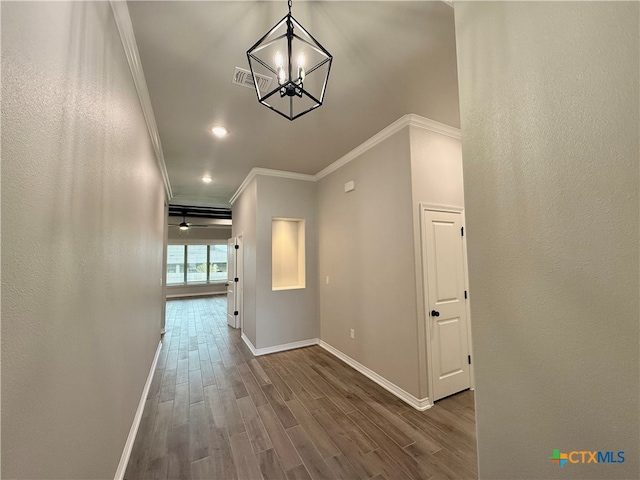 corridor with wood-type flooring, crown molding, and an inviting chandelier