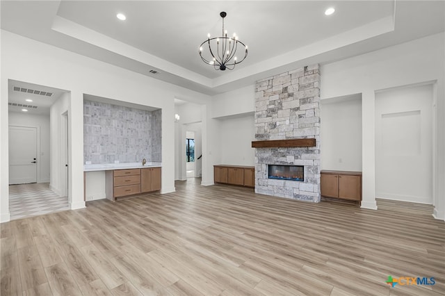 unfurnished living room with a fireplace, a tray ceiling, and light hardwood / wood-style flooring