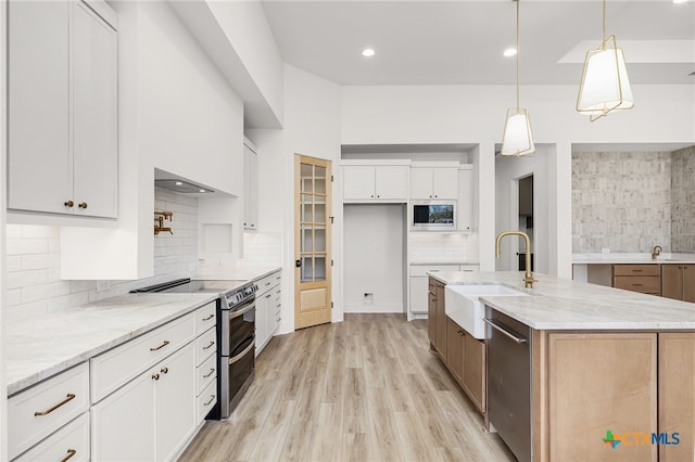 kitchen featuring stainless steel appliances, white cabinetry, sink, a center island with sink, and light stone countertops