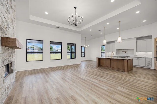 kitchen with a fireplace, a raised ceiling, pendant lighting, light wood-type flooring, and a large island with sink