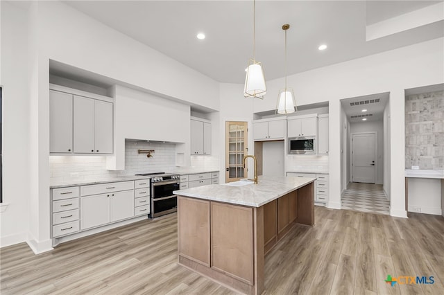 kitchen featuring stainless steel appliances, light hardwood / wood-style floors, a kitchen island with sink, light stone countertops, and white cabinetry