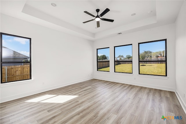 empty room featuring ceiling fan, light wood-type flooring, and a tray ceiling