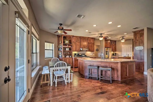 kitchen with light stone counters, a breakfast bar area, dark hardwood / wood-style flooring, a kitchen island with sink, and appliances with stainless steel finishes