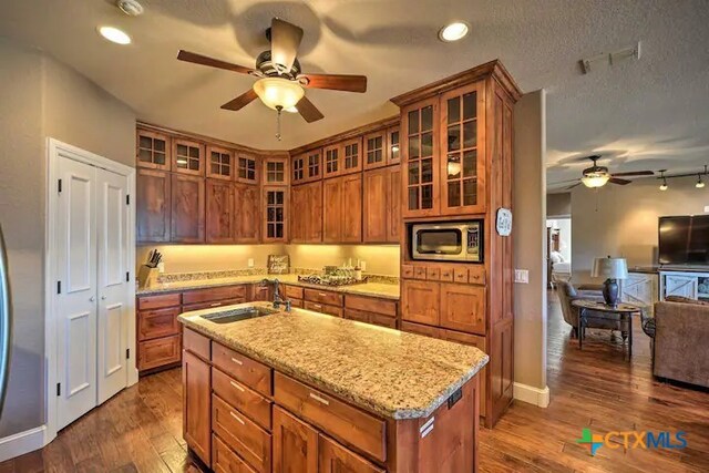 kitchen featuring sink, an island with sink, dark hardwood / wood-style floors, and stainless steel microwave