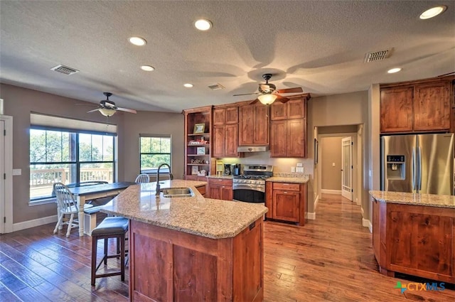 kitchen featuring a kitchen island with sink, stainless steel appliances, a textured ceiling, light stone counters, and sink