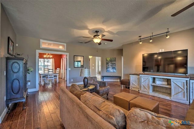 living room with ceiling fan with notable chandelier, a textured ceiling, rail lighting, and dark hardwood / wood-style floors