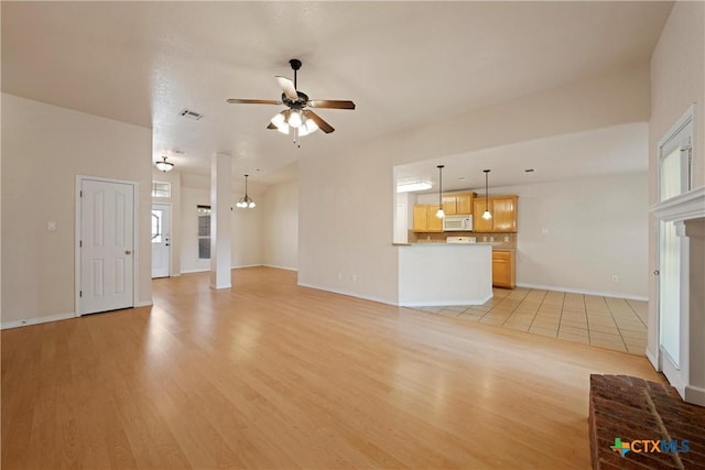 unfurnished living room with ceiling fan with notable chandelier and light hardwood / wood-style floors