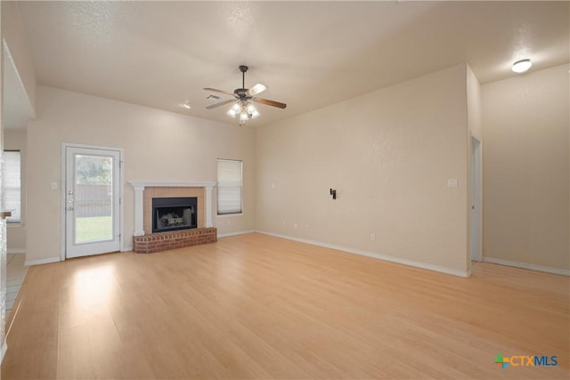 unfurnished living room with ceiling fan, a brick fireplace, and light hardwood / wood-style flooring