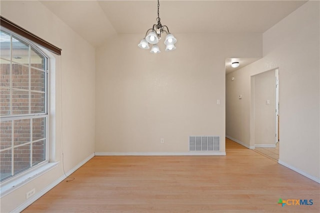 spare room with an inviting chandelier, vaulted ceiling, and light hardwood / wood-style floors