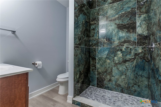 bathroom with hardwood / wood-style floors, vanity, toilet, and tiled shower