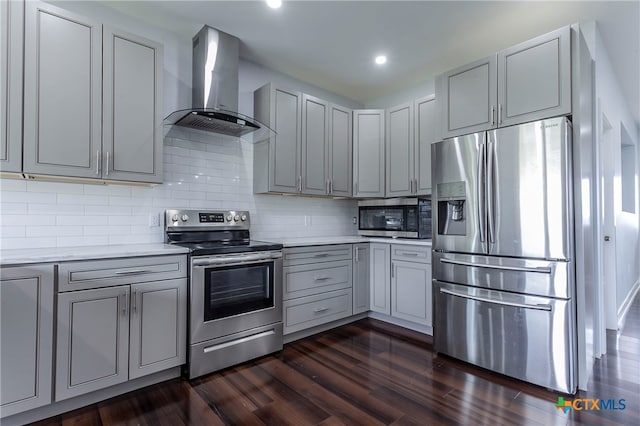 kitchen featuring gray cabinetry, tasteful backsplash, stainless steel appliances, wall chimney range hood, and dark wood-type flooring