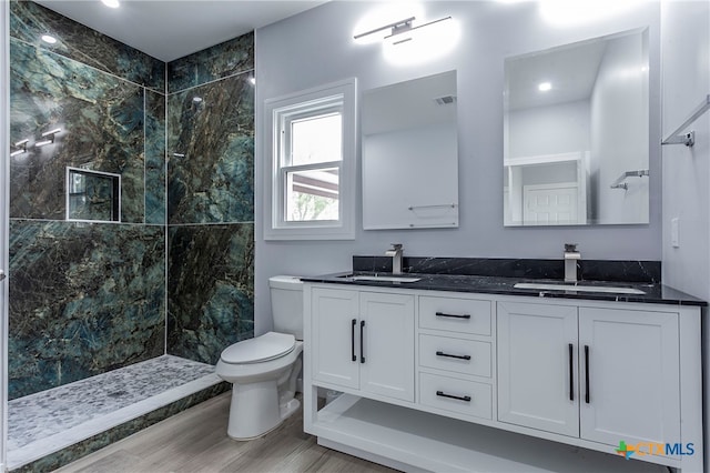 bathroom with hardwood / wood-style flooring, vanity, toilet, and a tile shower