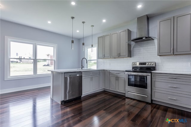 kitchen featuring sink, appliances with stainless steel finishes, wall chimney exhaust hood, gray cabinets, and pendant lighting