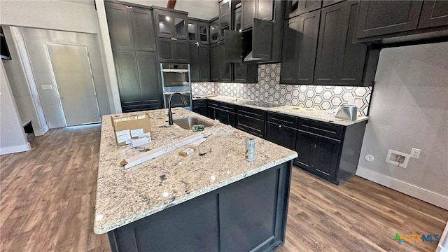 kitchen with light stone counters, hardwood / wood-style floors, sink, black stovetop, and double oven