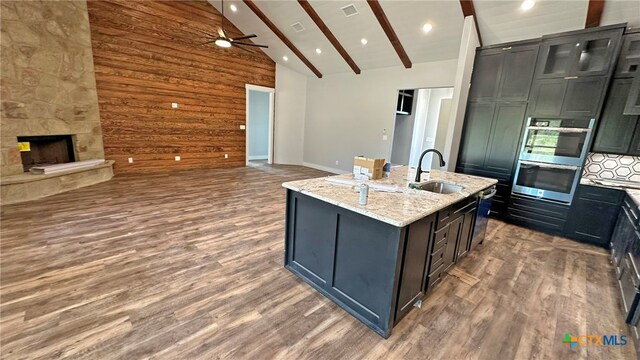 kitchen with dark hardwood / wood-style flooring, beamed ceiling, light stone counters, and an island with sink