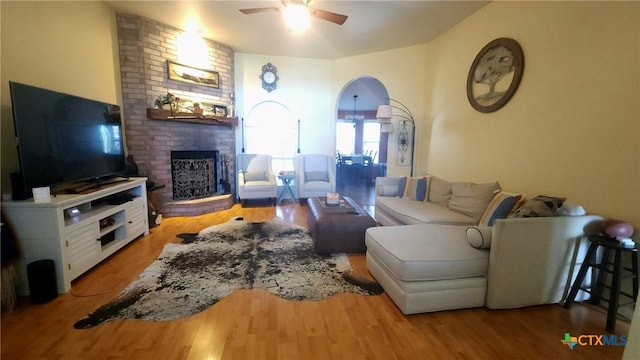 living room with ceiling fan, wood-type flooring, and a brick fireplace