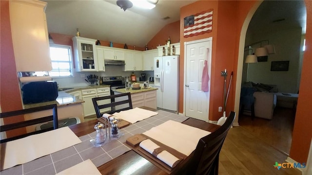 kitchen featuring electric range, white refrigerator with ice dispenser, light hardwood / wood-style floors, lofted ceiling, and white cabinets