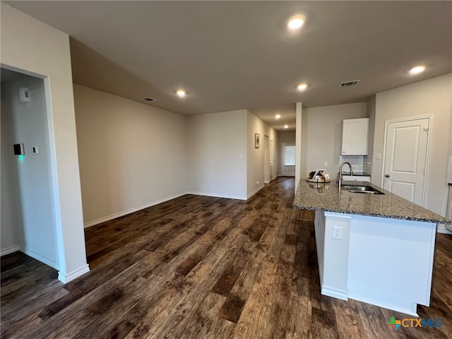 kitchen with sink, dark stone counters, dark hardwood / wood-style floors, an island with sink, and white cabinets