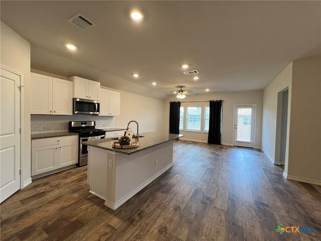 kitchen with stainless steel appliances, white cabinetry, sink, dark wood-type flooring, and a kitchen island with sink