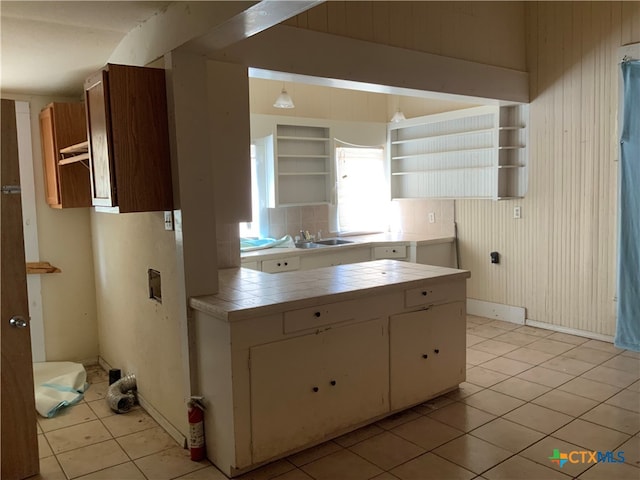 kitchen featuring tile countertops, light tile patterned floors, sink, wooden walls, and white cabinetry