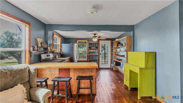 kitchen with stainless steel appliances, dark wood-type flooring, kitchen peninsula, ceiling fan, and a breakfast bar