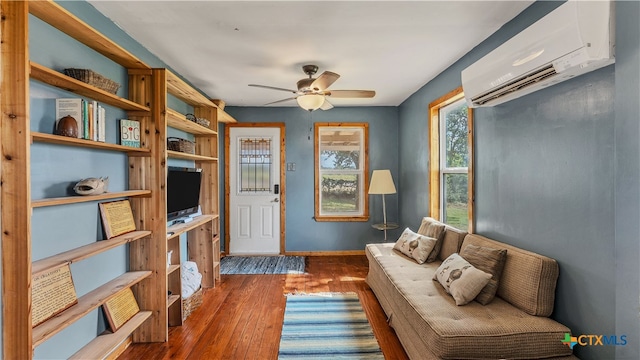 sitting room with dark wood-type flooring, a wall unit AC, and ceiling fan