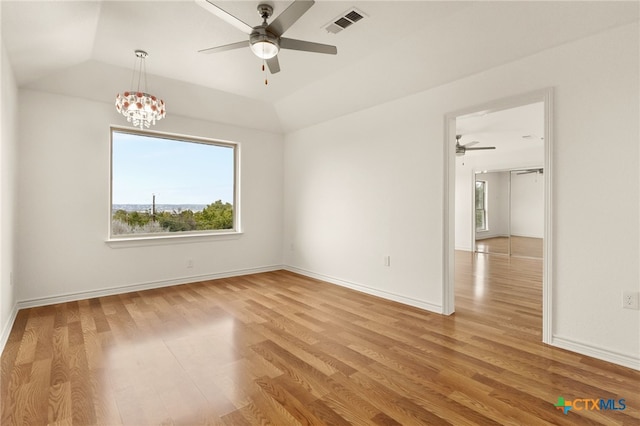 spare room featuring ceiling fan with notable chandelier, vaulted ceiling, and light hardwood / wood-style flooring