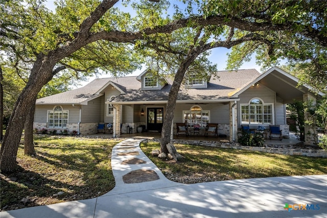 view of front of house with covered porch, a shingled roof, stone siding, french doors, and a front lawn