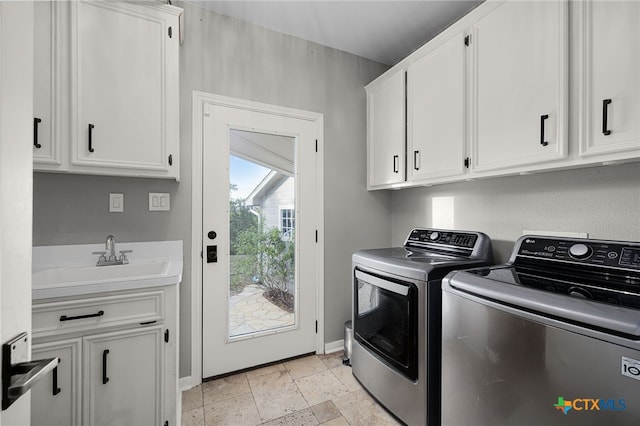 laundry area featuring separate washer and dryer, cabinet space, stone tile flooring, a sink, and baseboards