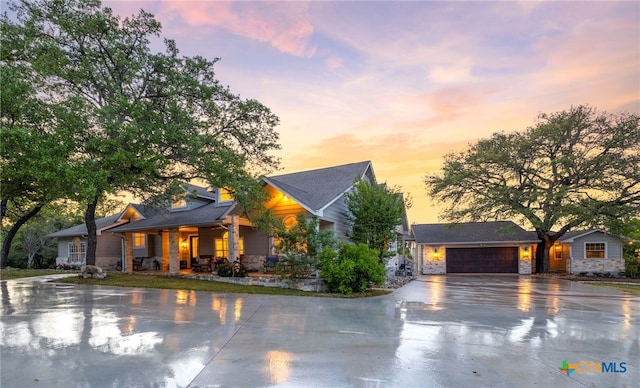 view of front of house with driveway, a porch, an attached garage, and stone siding