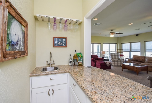 kitchen with white cabinets, light stone counters, ceiling fan, and sink