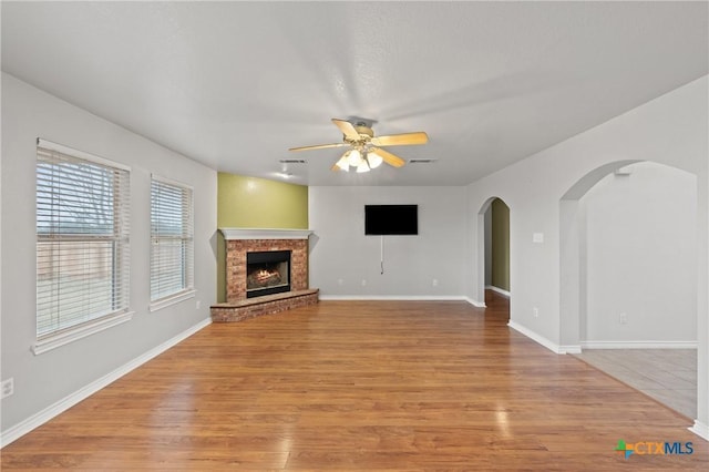 unfurnished living room with a brick fireplace, light hardwood / wood-style flooring, and ceiling fan