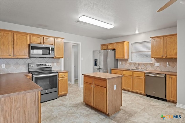 kitchen with sink, ceiling fan, stainless steel appliances, tasteful backsplash, and a kitchen island