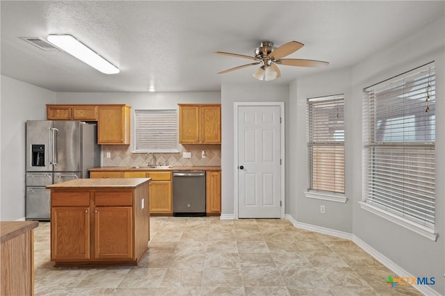 kitchen with appliances with stainless steel finishes, sink, backsplash, a center island, and ceiling fan