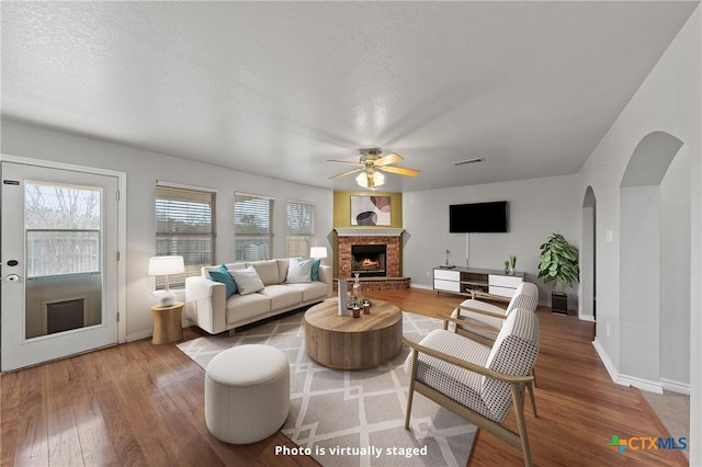 living room featuring ceiling fan, hardwood / wood-style floors, a brick fireplace, and a textured ceiling