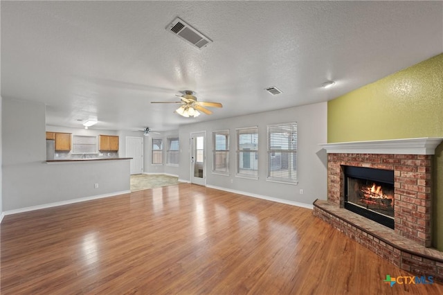 unfurnished living room with ceiling fan, a fireplace, light hardwood / wood-style floors, and a textured ceiling