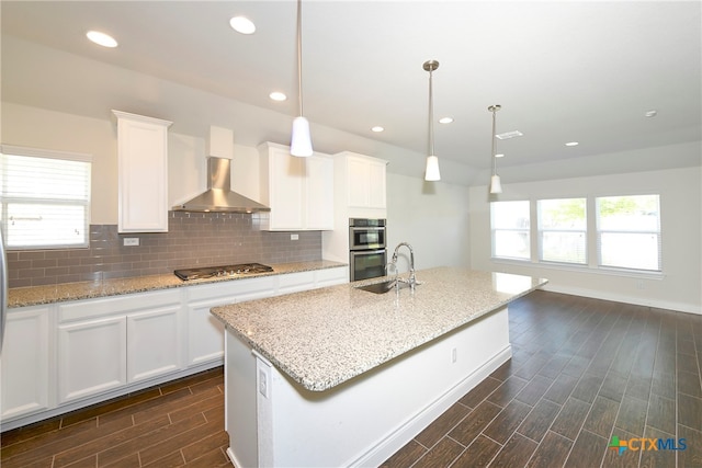 kitchen featuring wall chimney range hood, white cabinetry, and decorative light fixtures